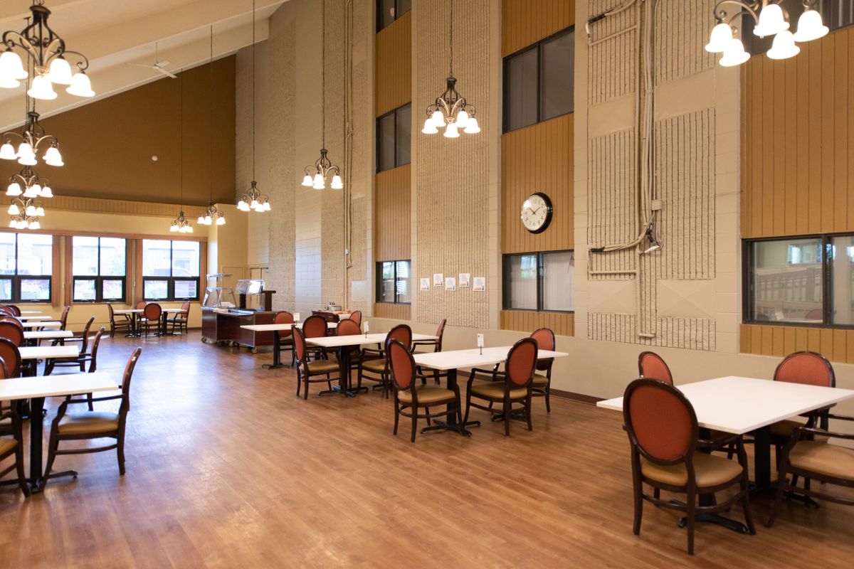 A spacious dining area with high ceilings, featuring tables and chairs on a wooden floor.