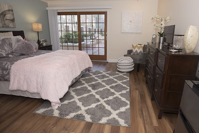 A cozy bedroom featuring a large rug, wooden flooring, and elegant furniture.