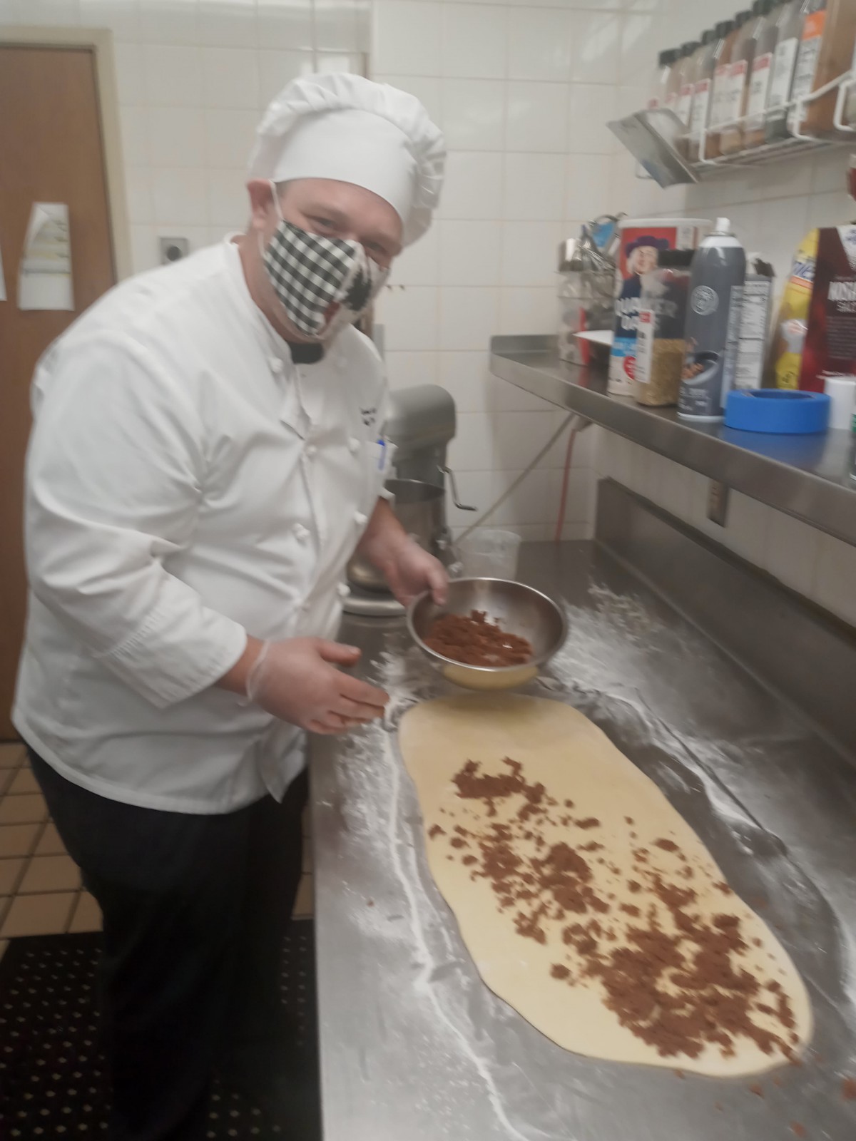 A chef preparing dough with toppings in a commercial kitchen.