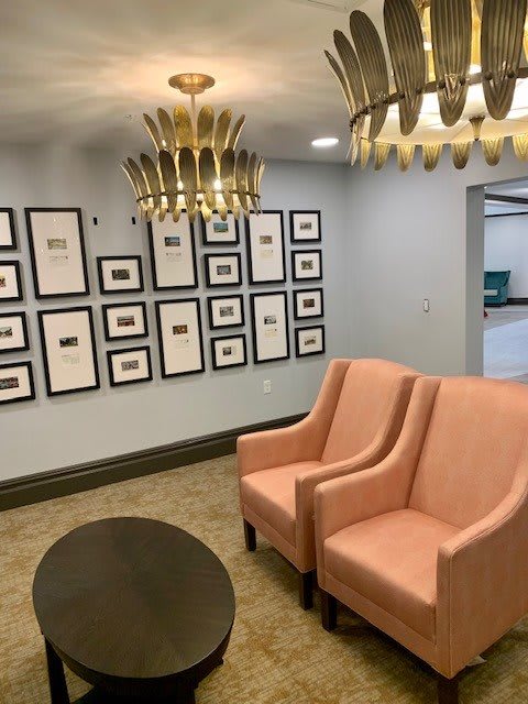 A modern waiting room featuring pink chairs, decorative chandeliers, and a gallery wall of framed artwork.