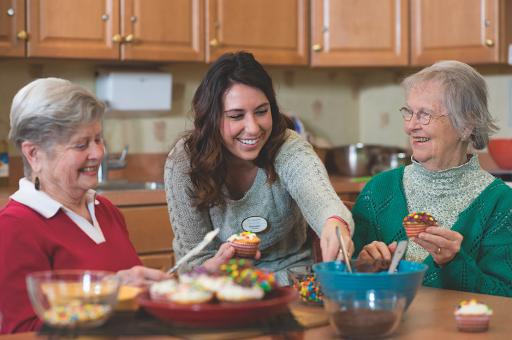 A caregiver shares a joyful moment with elderly individuals while preparing desserts in the kitchen.