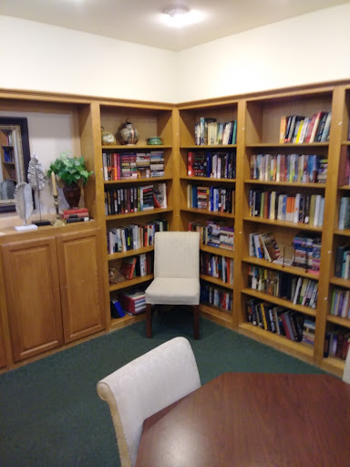 A cozy corner of a library featuring wooden bookshelves filled with various books and a comfortable chair.