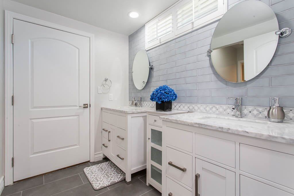 A modern bathroom with white cabinetry, round mirrors, and decorative blue flowers.