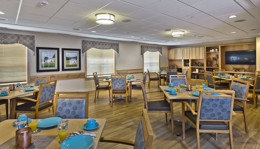 An inviting dining room with tables and chairs neatly arranged, featuring blue dishware and warm lighting.