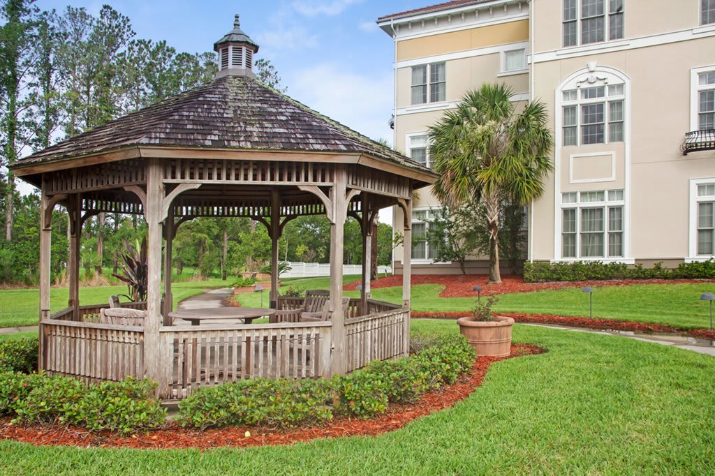 A charming gazebo situated next to a residential building, surrounded by well-manicured lawns and lush landscaping.