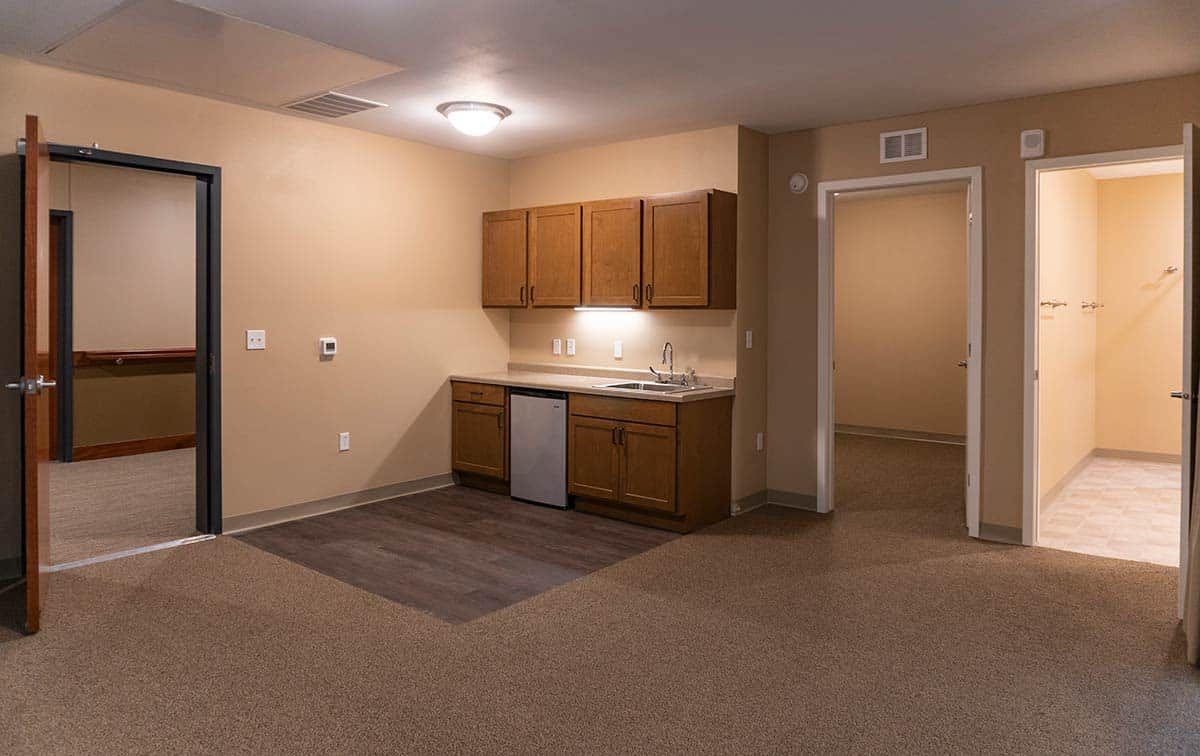 A minimalist kitchen area with brown cabinets and beige walls in an empty apartment.