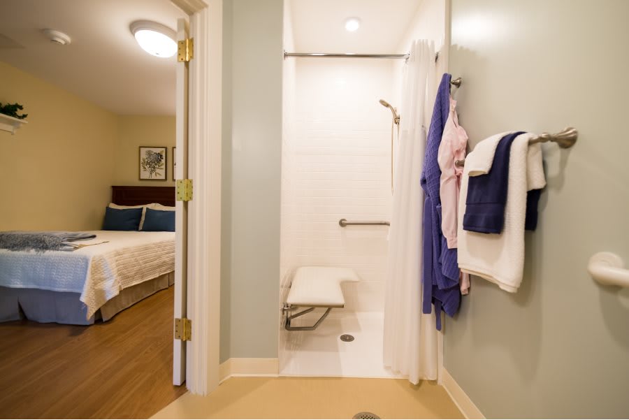 An accessible bathroom featuring a shower with a folding seat, adjacent to a hotel bedroom.