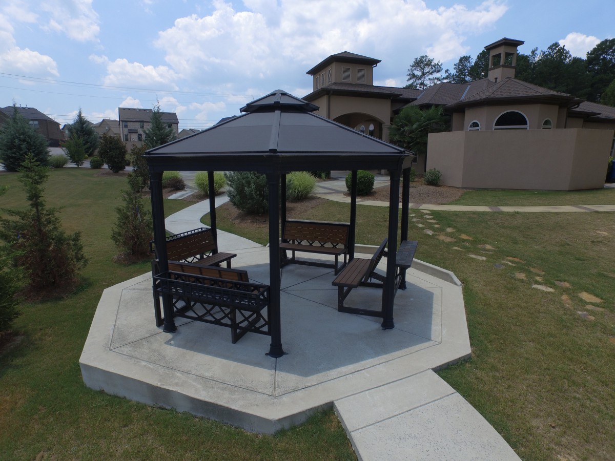 A gazebo with benches situated in a landscaped outdoor area near buildings.