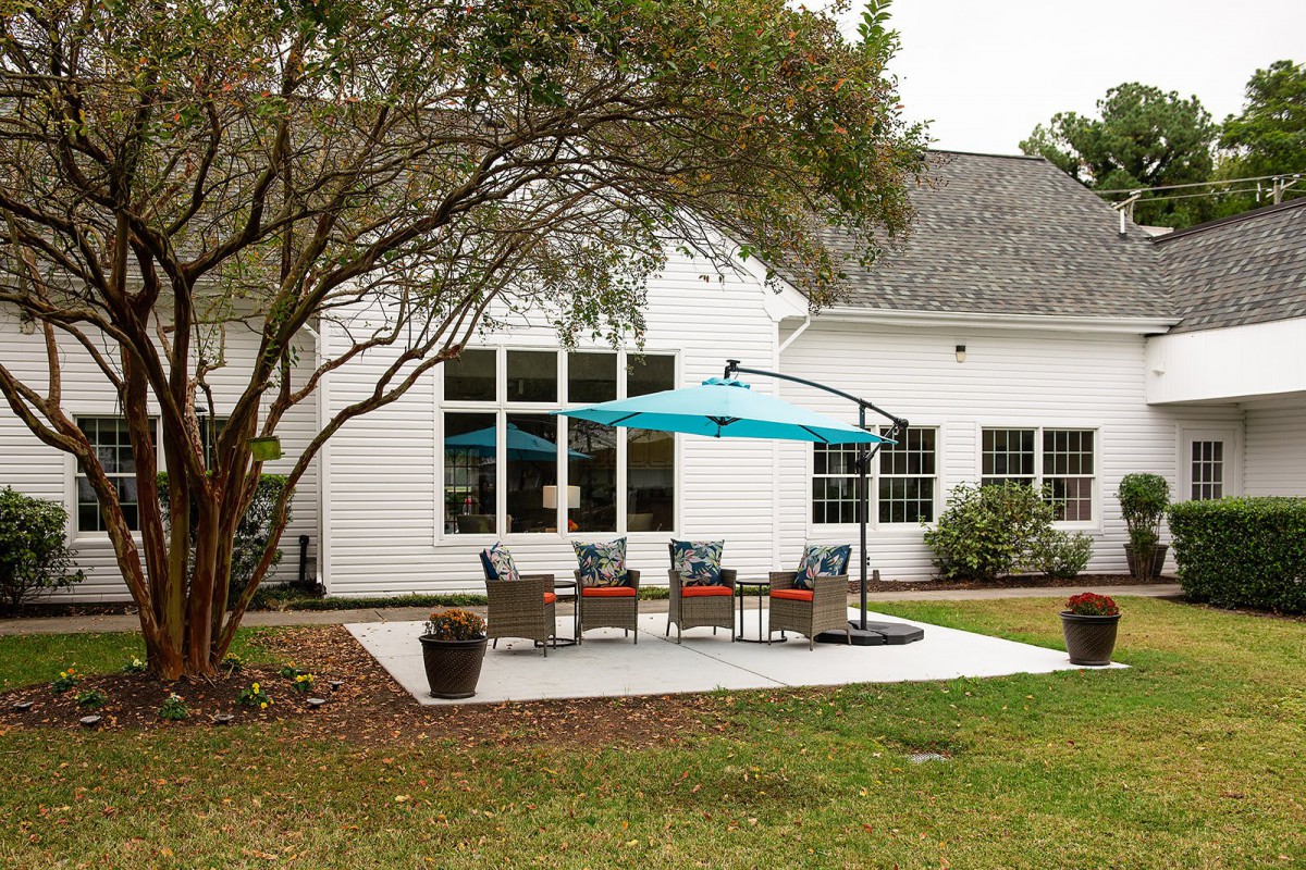 A cozy backyard patio setup with chairs under a blue umbrella beside a white house.