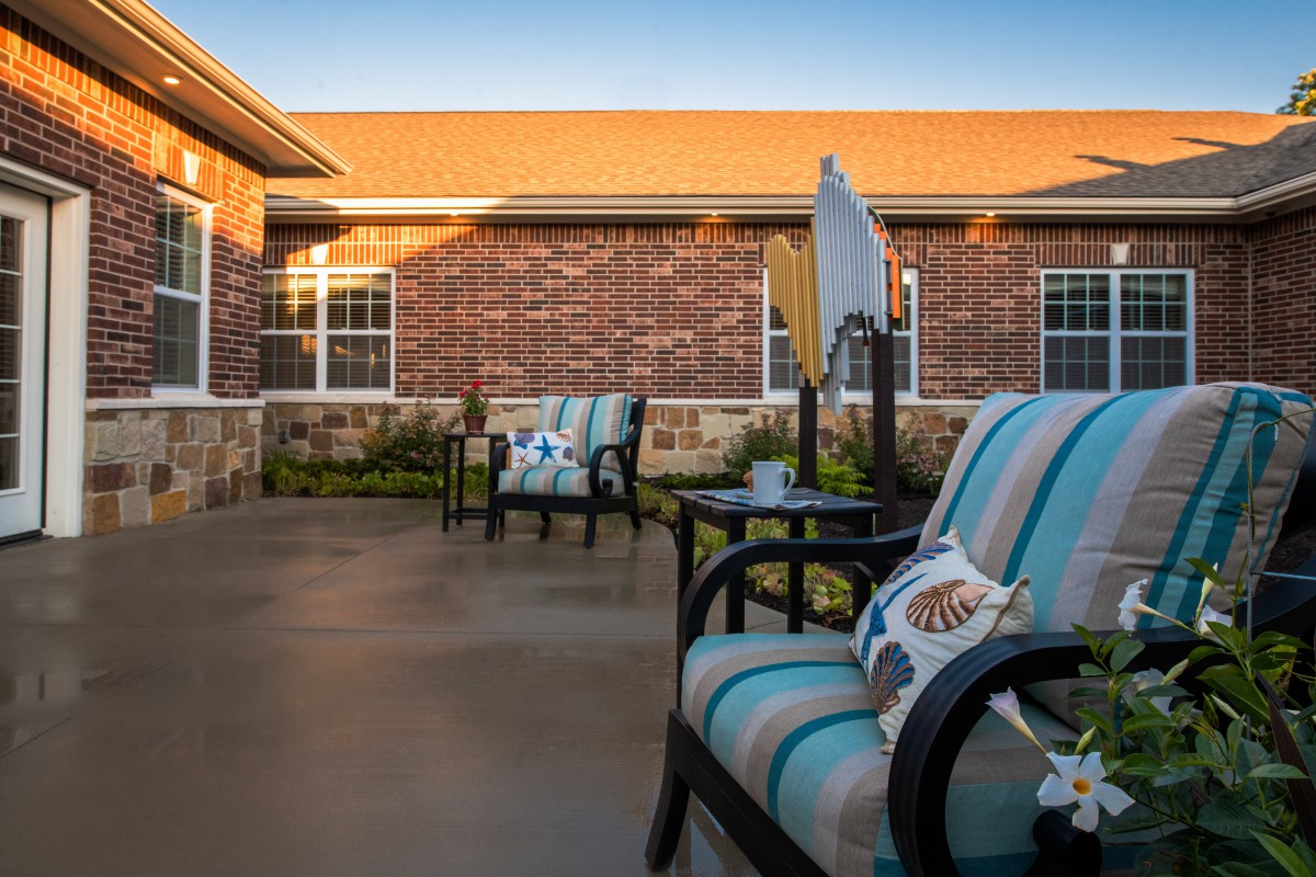 A cozy patio area with cushioned chairs against a brick building during sunset.