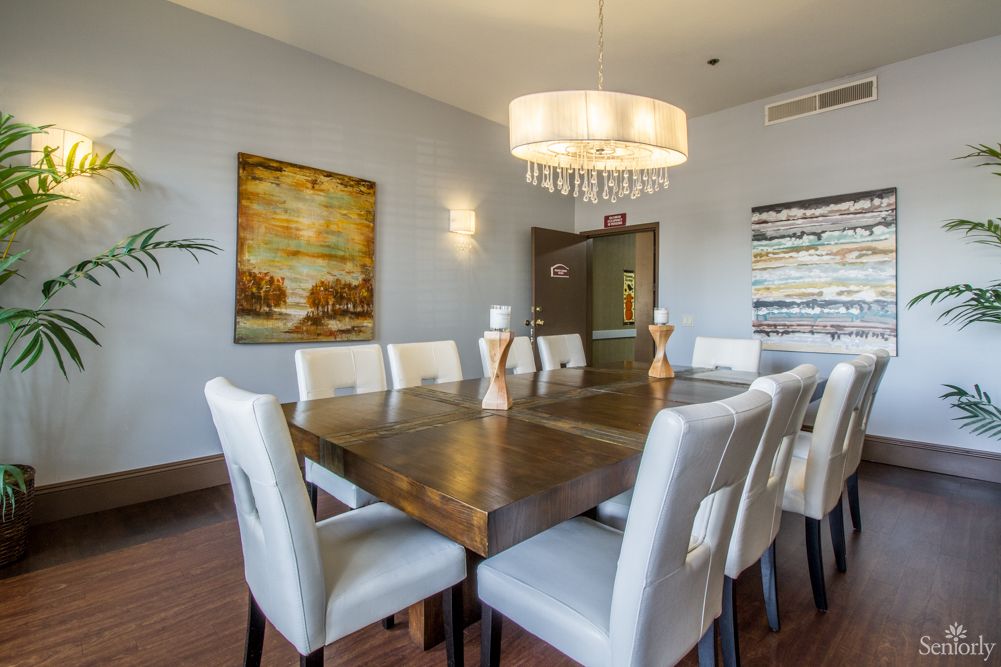 A stylish dining room featuring a large wooden table surrounded by white chairs, with a modern chandelier overhead and wall art decorating the space.