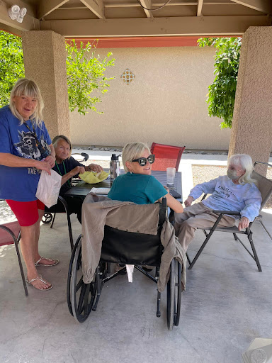 A group of people enjoying a sunny day outdoors, with caregivers attending to elderly individuals.