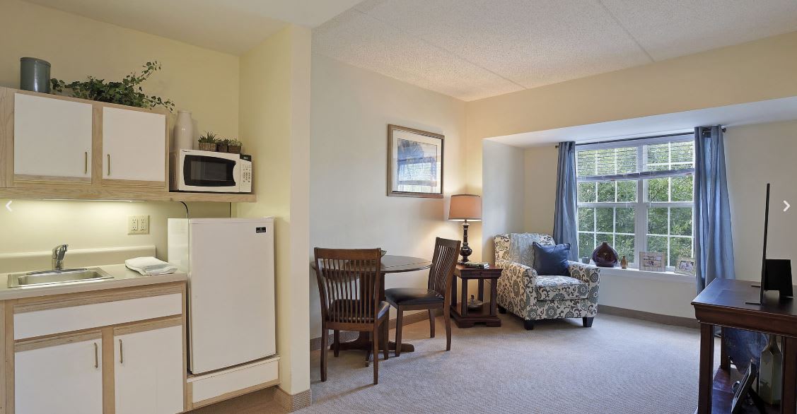 A cozy living room with a small dining area, featuring a table, chairs, lamp, and a microwave in the corner.