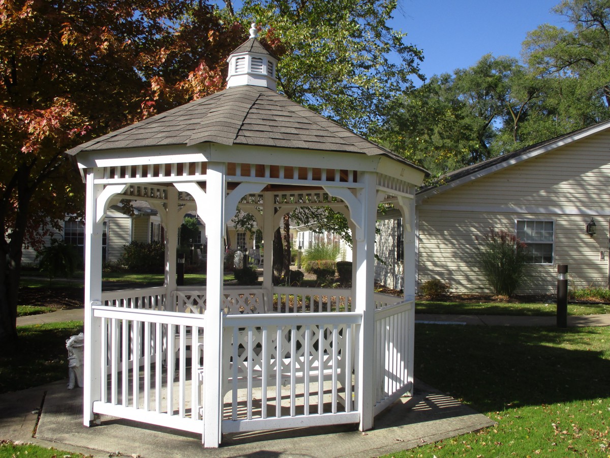 A white wooden gazebo in a garden setting.