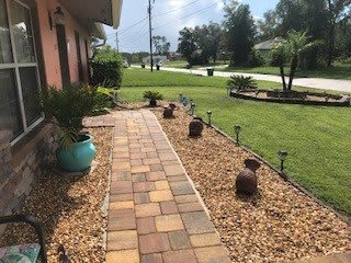 A landscaped front yard featuring a paved pathway surrounded by pebbles and plants.