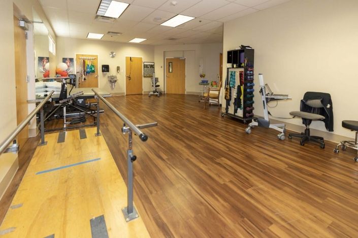 A spacious rehabilitation room equipped with therapy rails and various gym equipment.
