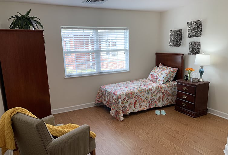 A cozy bedroom with a single bed, dresser, and armchair by the window.