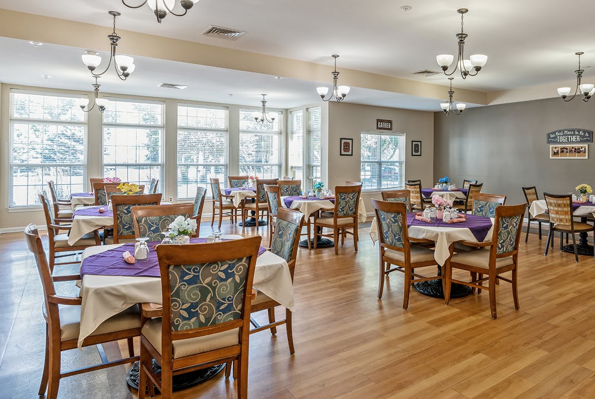 A well-decorated dining room with multiple tables set up, featuring hardwood flooring and large windows.