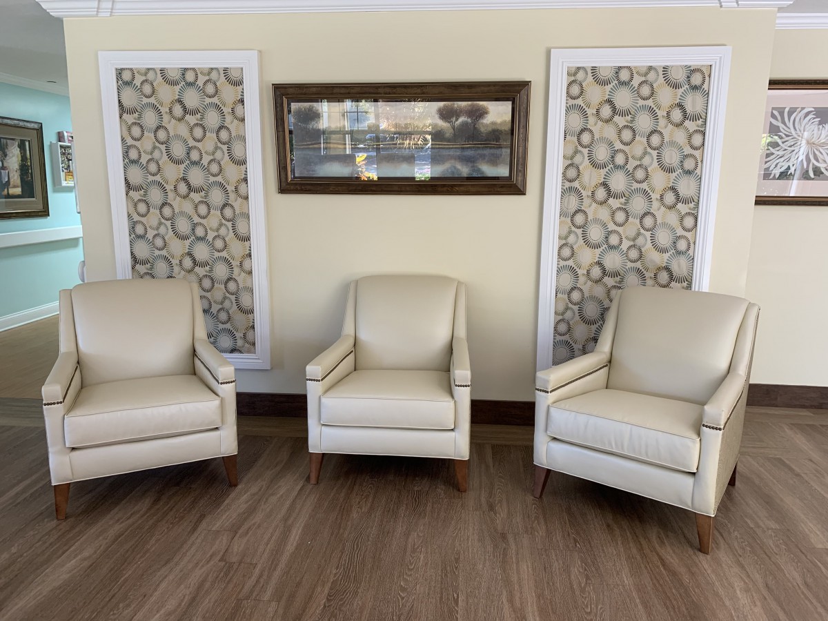 A cozy living room setup featuring three beige armchairs, decorative wall art, and a wooden floor.
