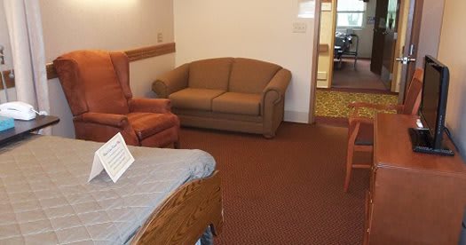 A cozy living room with a brown sofa, an armchair, and carpeted flooring.