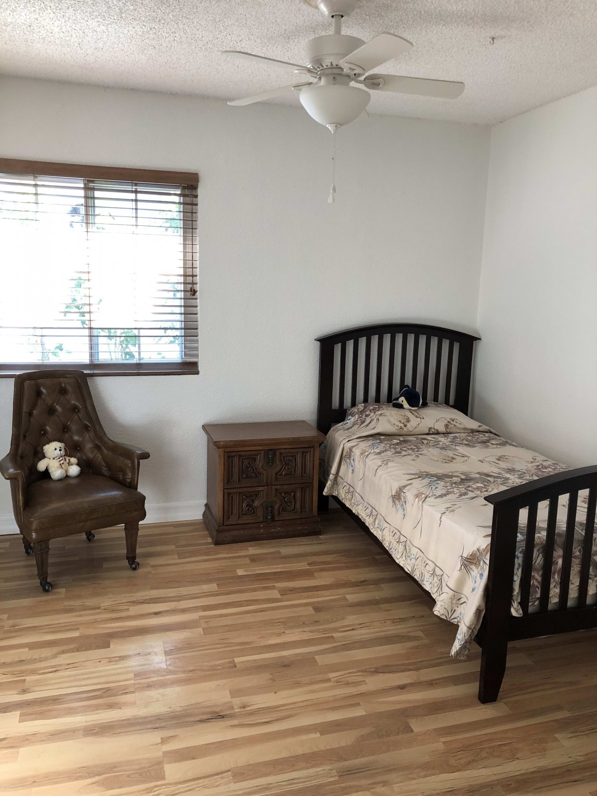 A simple bedroom with a single wooden bed, nightstand, and chair on a wooden floor.