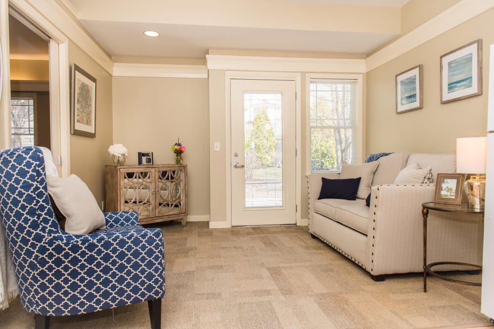 A cozy living room with a sofa, chair, and hardwood flooring, featuring a door leading outside.