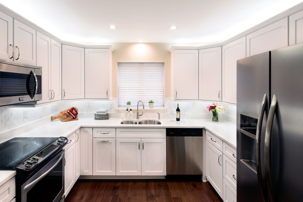 A modern kitchen with white cabinets, stainless steel appliances, and hardwood flooring.