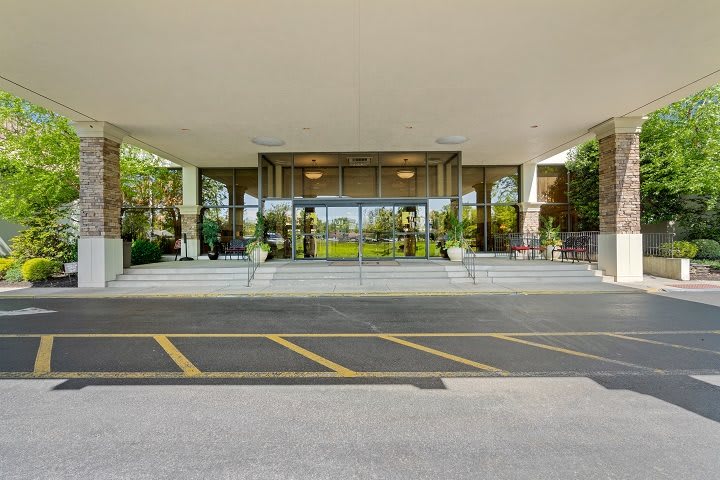The entrance features glass doors, front steps, and potted plants beneath a large awning.