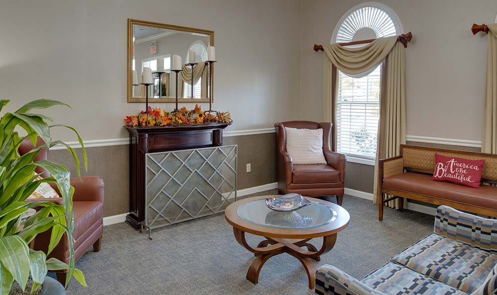 A cozy living room with elegant furnishings, featuring an armchair, a small round table, and a decorative mirror above a mantelpiece.