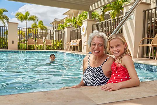A woman and a young girl enjoying time by the pool on a sunny day.