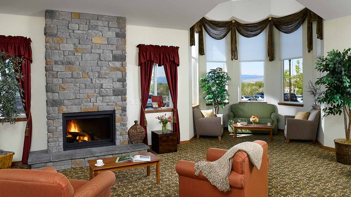 A cozy living room with a stone fireplace, comfortable armchairs, and large windows showcasing an inviting view.