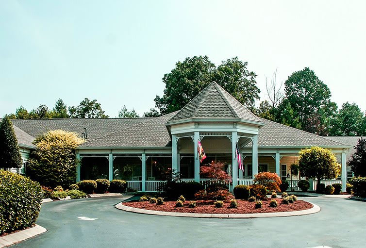 A charming building with a landscaped garden and circular driveway, surrounded by trees.