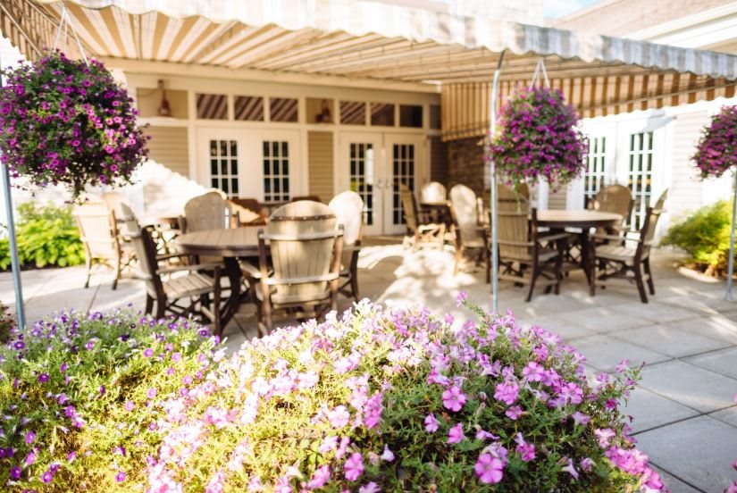A sunny outdoor patio at a restaurant with tables, chairs, and vibrant flowers.