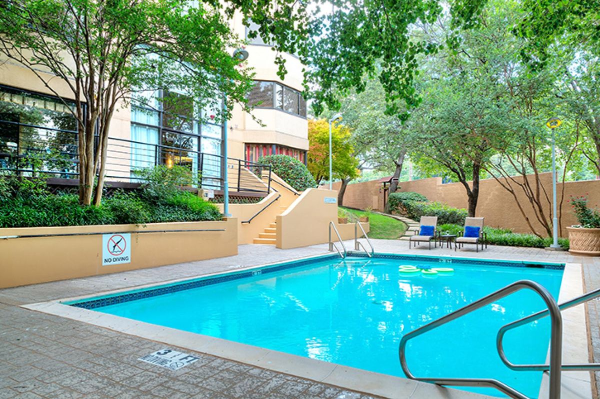 A serene outdoor swimming pool area surrounded by greenery at an apartment complex.