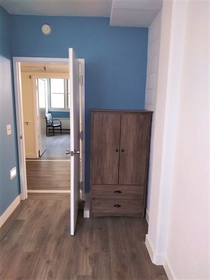 A hallway with a blue wall, featuring an open door and a wooden wardrobe.