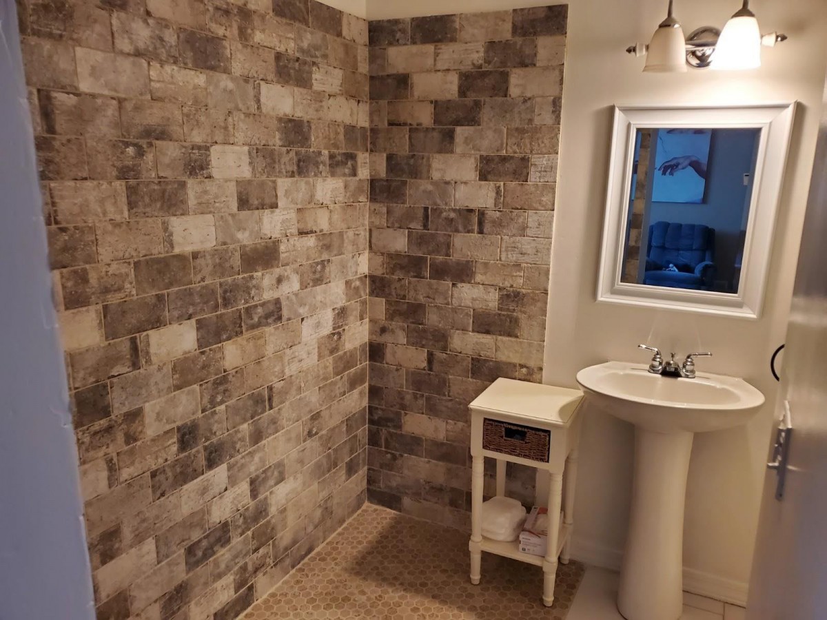 A stylish bathroom featuring a tiled wall, pedestal sink, and framed mirror.
