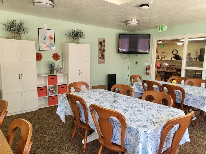 A neatly arranged dining room with a long table, wooden chairs, decorative elements on the walls, and a television mounted on the wall.