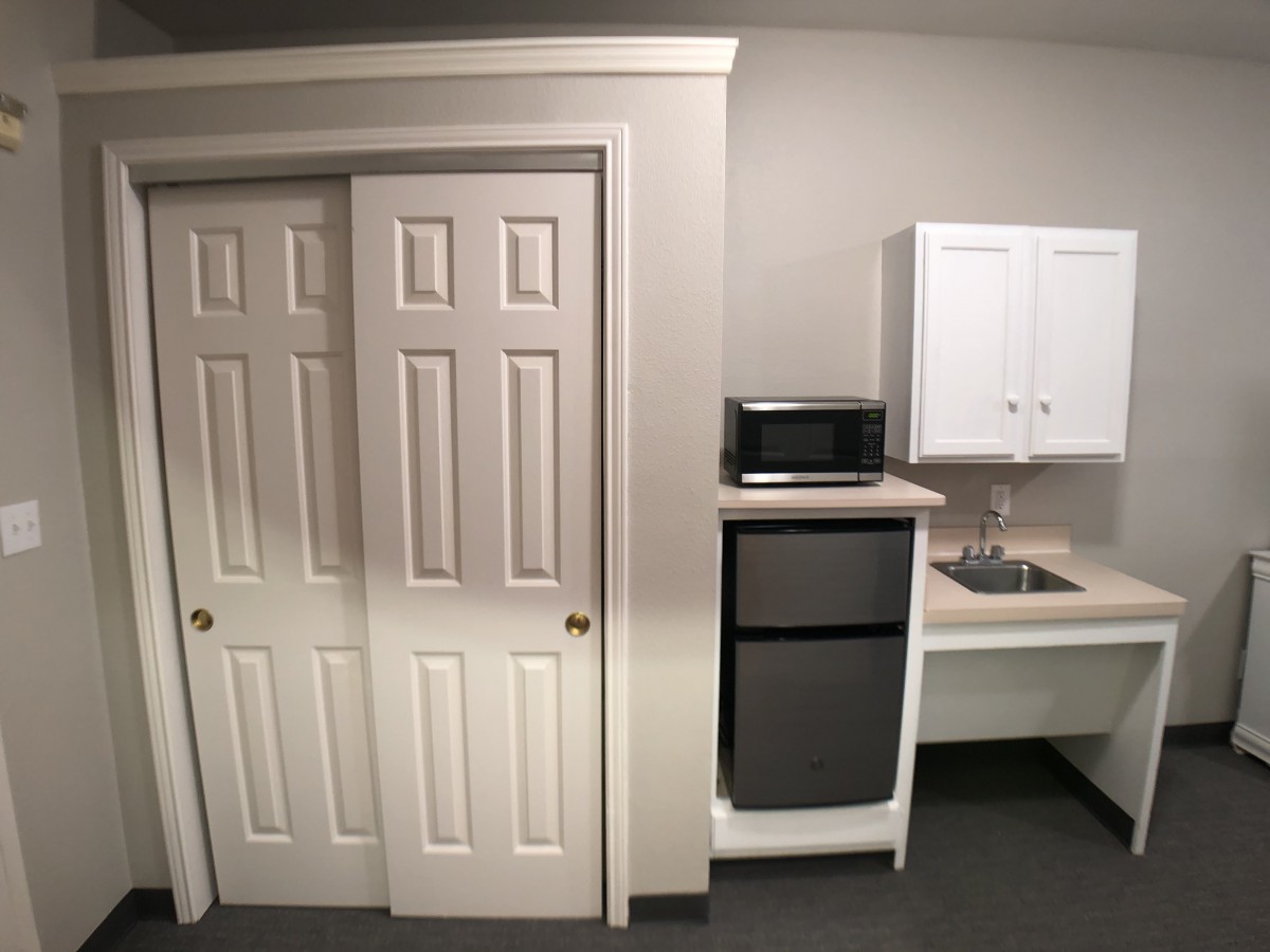 A compact kitchenette featuring a refrigerator, microwave, sink, and storage cabinets.