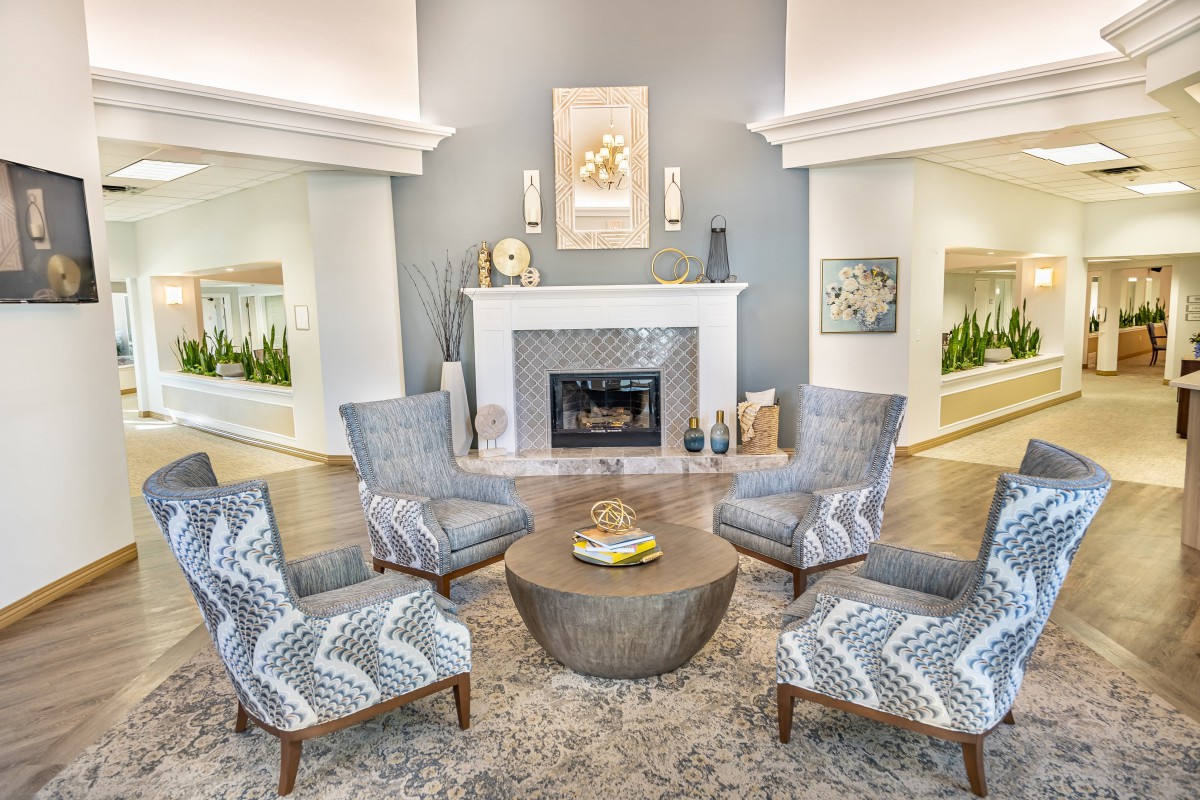 A modern living room featuring a central fireplace, surrounded by patterned chairs and a round wooden table.