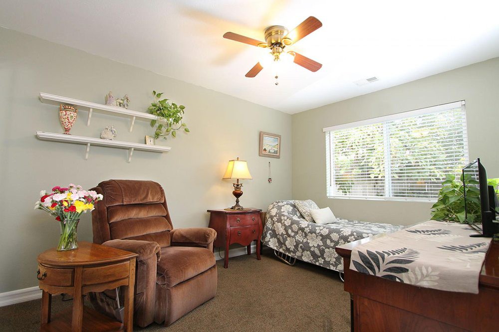 A cozy bedroom featuring a single bed, comfortable armchair, and decorative elements like plants and a ceiling fan.