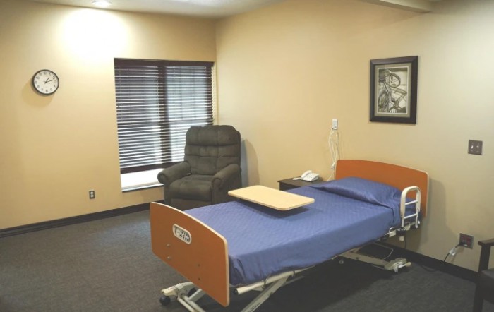 An empty hospital room with a bed and a chair next to a window.