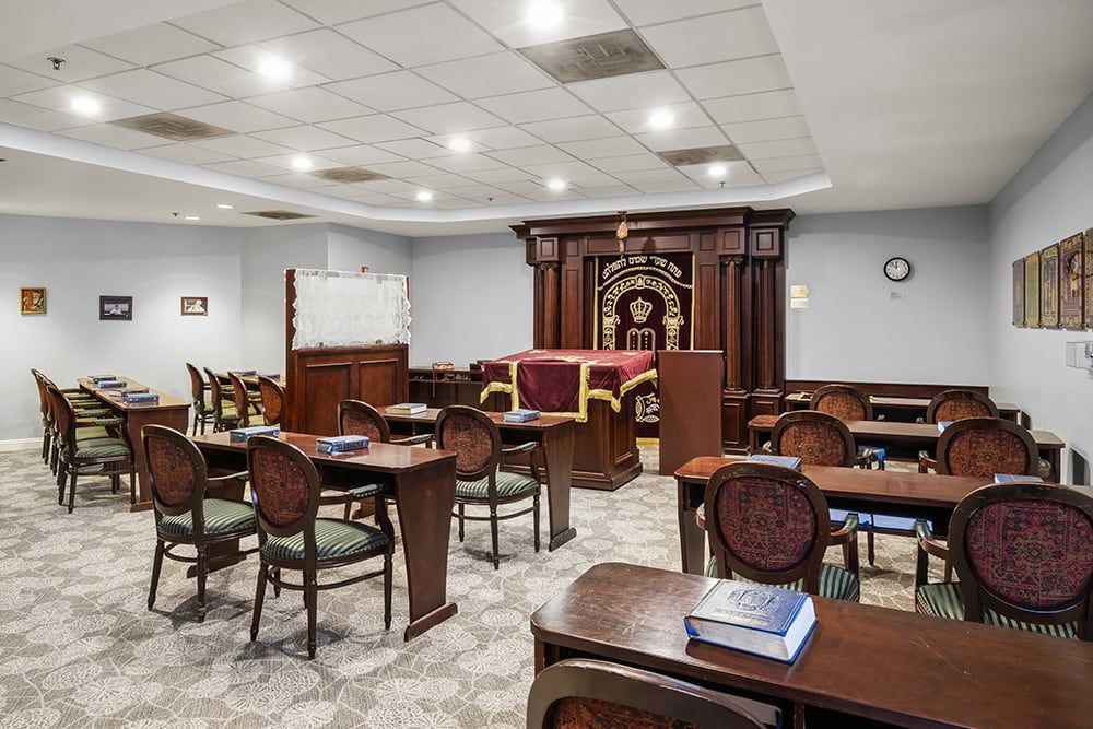 Interior view of a synagogue prayer room with arranged seating and a Torah ark at the front.