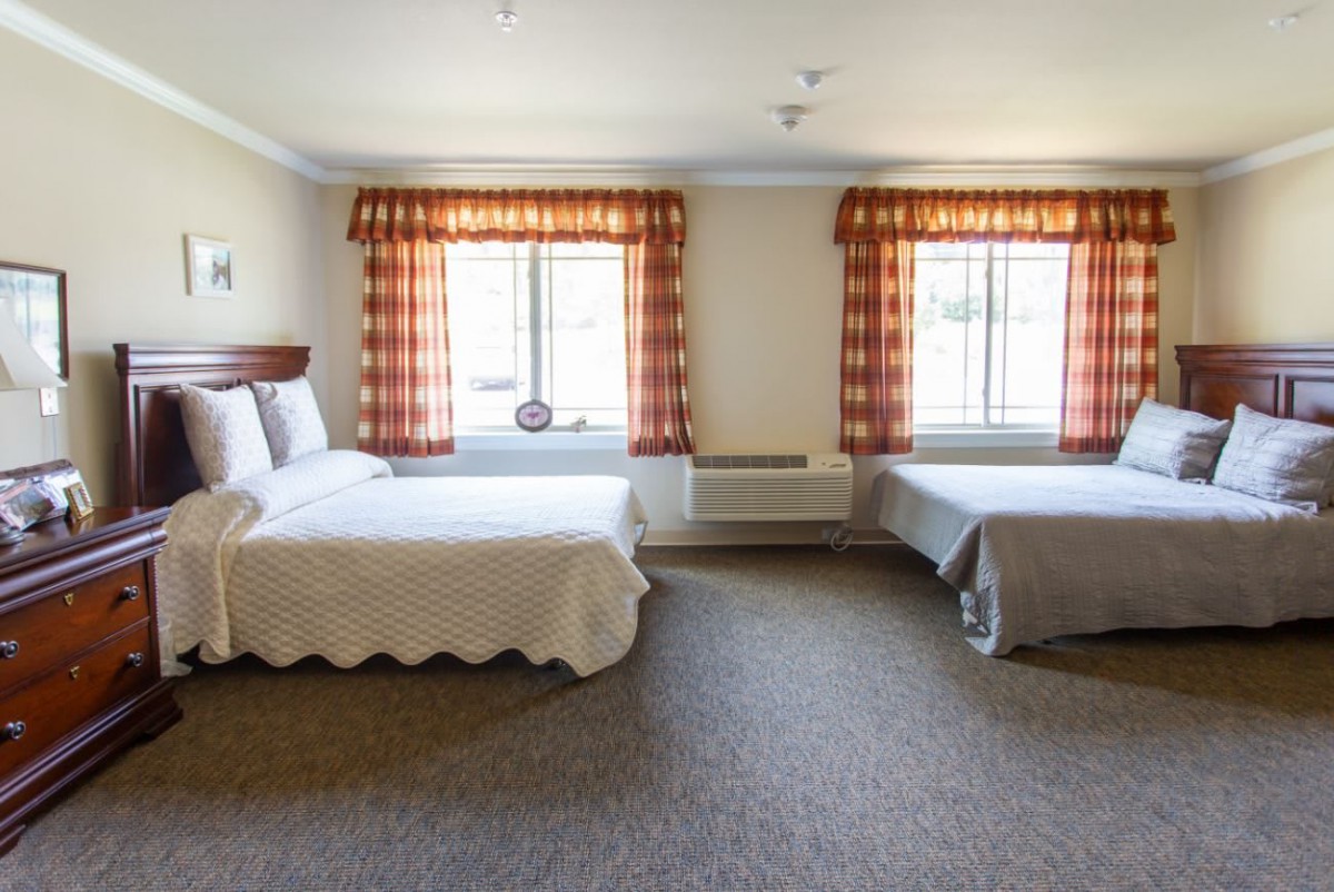 A spacious hotel room featuring two double beds and warmly decorated curtains.