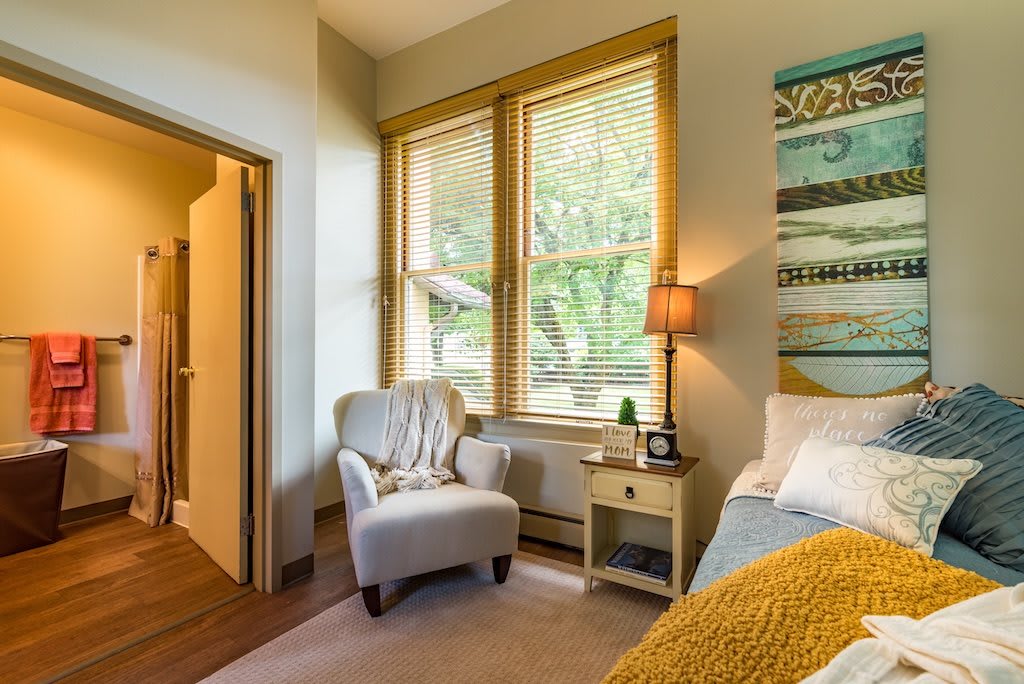 A cozy bedroom with an armchair by the window and soft lighting from a lamp.