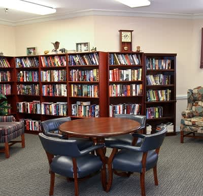 A cozy reading area in a library with bookshelves and a round table surrounded by chairs.