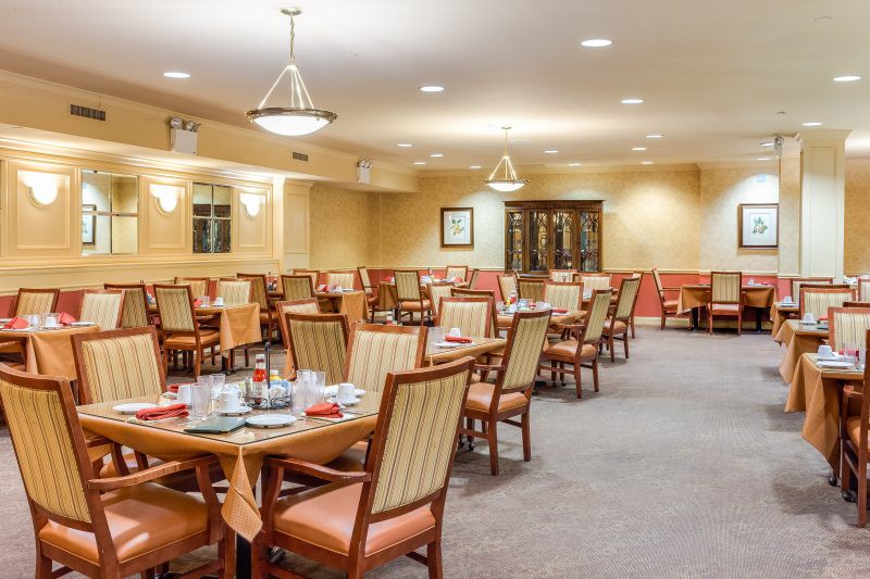 An empty dining room with neatly arranged tables and chairs, featuring warm lighting and a carpeted floor.