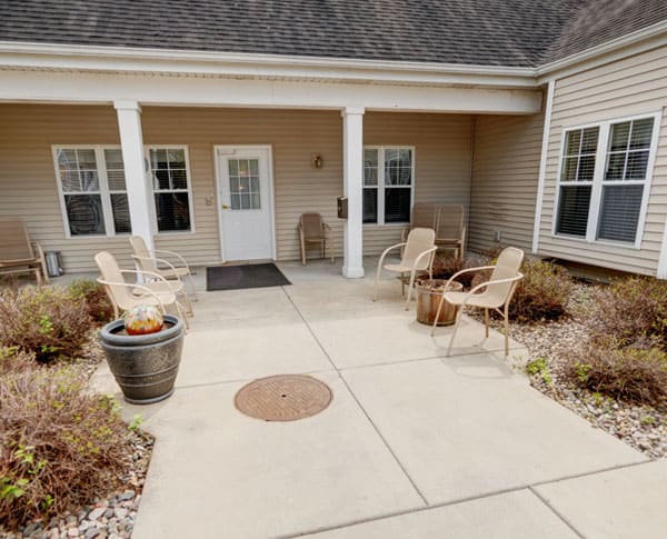 A cozy outdoor patio area with chairs and plants at the entrance of a building.