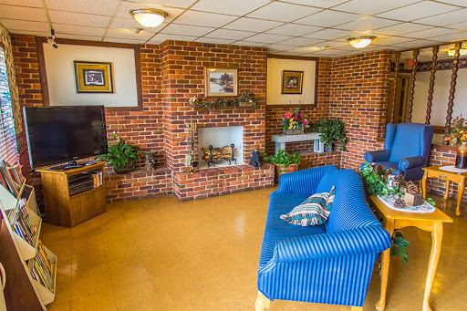 A cozy living room featuring a brick fireplace, blue sofa, and various plants.