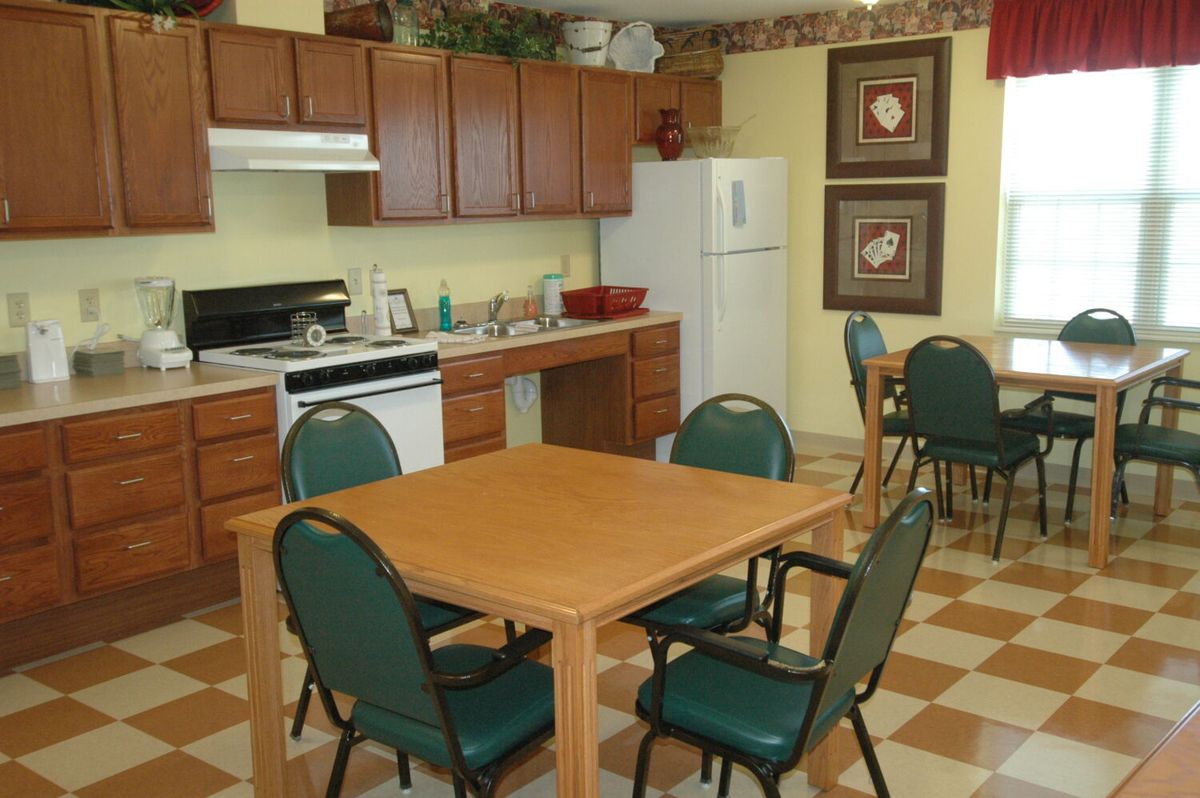 A communal kitchen and dining area featuring a table with chairs, wooden cabinets, and standard appliances including a refrigerator and stove.