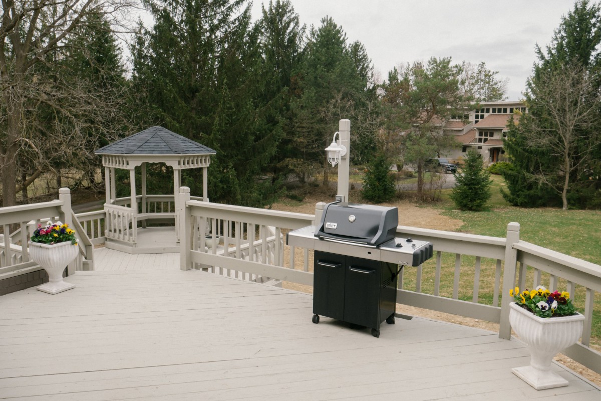 An outdoor deck with a grill and gazebo, surrounded by trees.